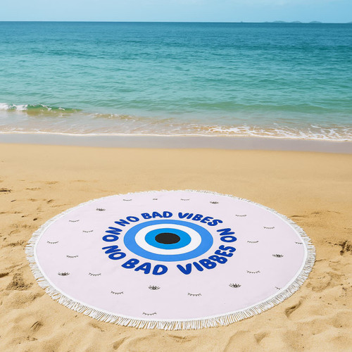 A round beach towel in light pink, featuring an eye design and fringe edges, with a logo present.