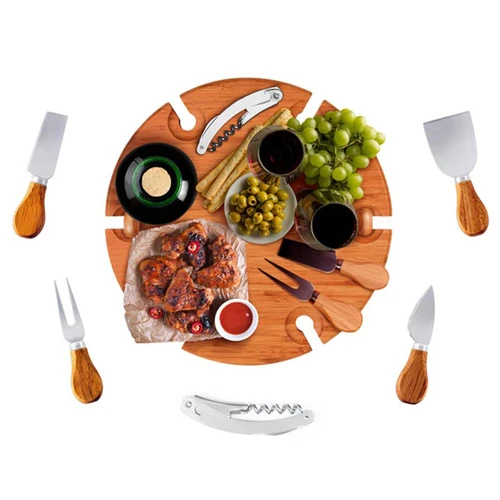 A wooden circular serving board features cheese, fruits, wine, and utensils, surrounded by knives and a corkscrew.