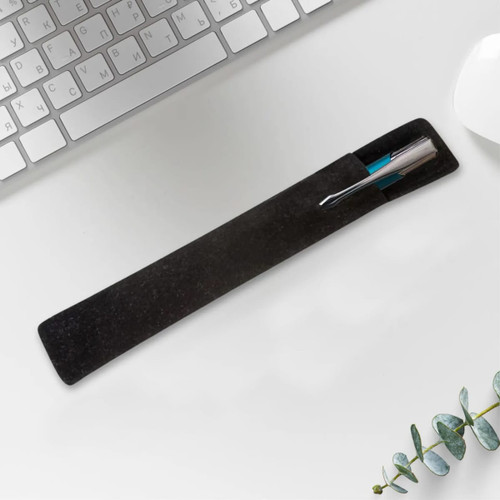 A black velvet pouch containing a pen, positioned on a desk with a keyboard and a plant.