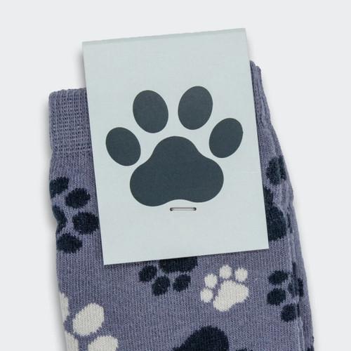A pair of knitted kids' socks in a purple-grey colour featuring a playful paw print design. Packaging has a paw badge.