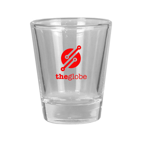 A clear glass shot glass with a solid base and a round logo in red and white.