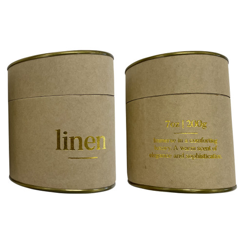 A large candle in a cylindrical kraft paper container with gold accents, labelled 'linen'.
