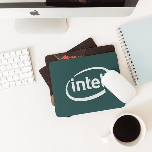 A green fabric mouse mat with a logo, placed on a desk alongside a white mouse, coffee cup, and notebook.