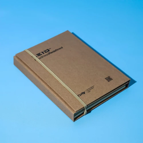 A brown A5 notepad secured with a rubber band, featuring a logo on the cover against a blue background.