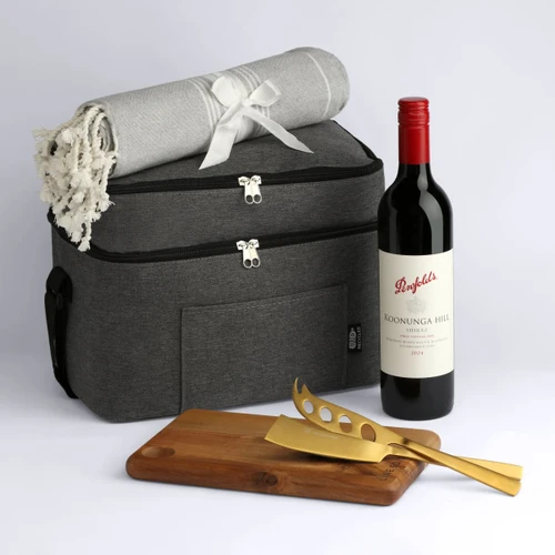 A cooler bag in grey with a blanket, a bottle of red wine, and wooden and gold utensils.
