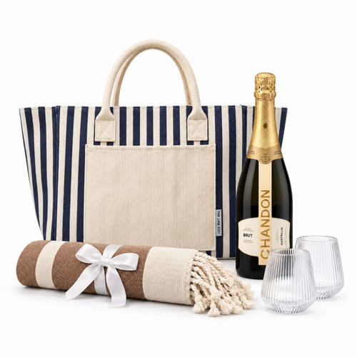 A striped tote bag, a bottle of Chandon Brut, two glasses, and a rolled blanket with a ribbon.