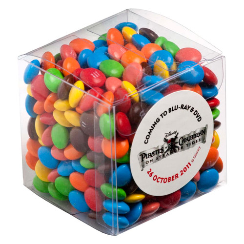 A clear cube filled with colourful chocolate-coated candy, including red, blue, yellow, green, and brown M&Ms.
