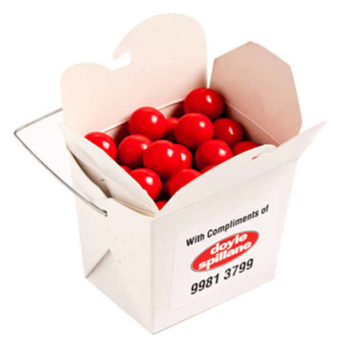 A white cardboard noodle box filled with bright orange chocolate drops. The box has a handle and a branding logo.