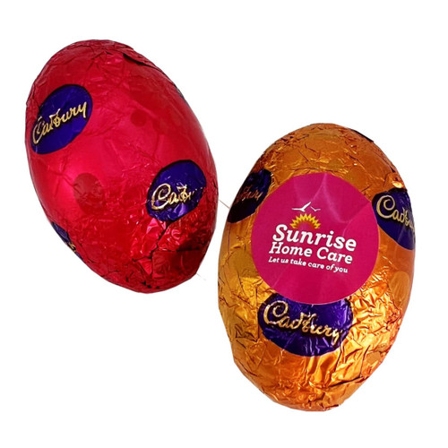 Two wrapped hollow chocolate Easter eggs in red and orange foil, featuring branding on one egg.