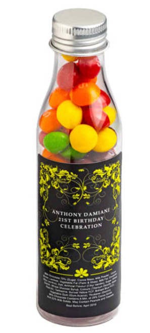 A drink bottle filled with colourful Skittles, featuring a metallic silver cap and decorative black and yellow label.