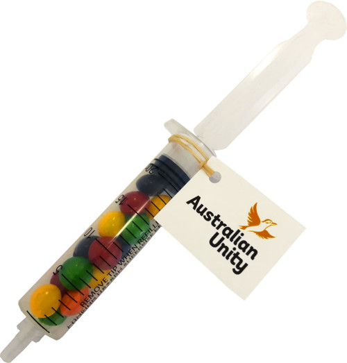 A syringe filled with vibrant Skittles in red, yellow, green, and purple, featuring a tag with a logo.