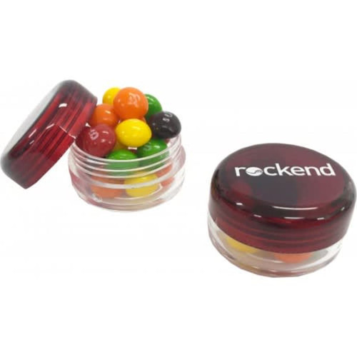 A small screw cap jar filled with colourful Skittles, featuring a red translucent lid and a logo on the front.