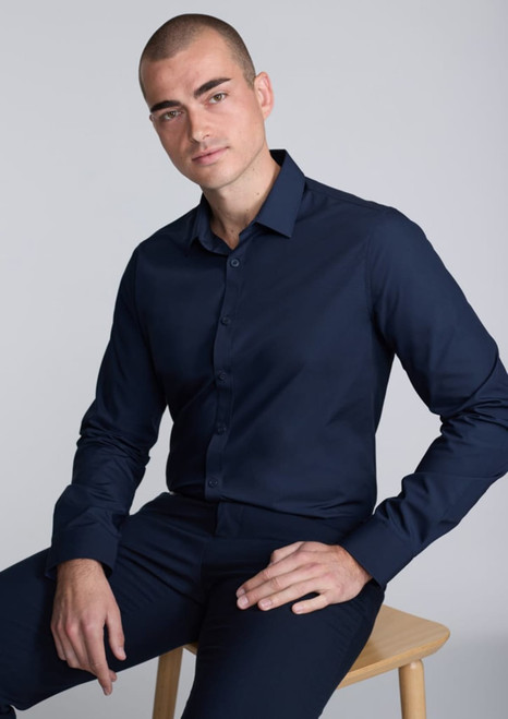 A slim fit long sleeve shirt in navy blue, worn by a man seated on a wooden chair, featuring a branding logo.