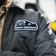A grey jacket featuring a custom woven patch with an off-road vehicle and mountain design.