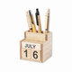 A wooden desk calendar with a drawer, featuring a day and month display, holding several writing instruments.