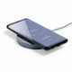 A wireless charger in grey with a smartphone placed on top, displaying a battery charging status on the screen.