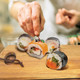 A wooden serving board displays sushi rolls, garnished with herbs, in a kitchen setting.