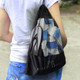 A black drawstring mesh bag with a logo, holding a drink bottle and other items, worn on the shoulder.