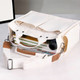 A cream canvas tote bag with straps and a structured design, partially filled with books and a camera.