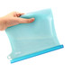 A silicone reusable storage pouch in a light blue colour, held by a hand, displaying its flexible design.