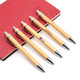Five eco bamboo pens with silver accents are arranged next to a red notebook, featuring a logo on the pens.