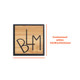 A custom-shaped bamboo lapel pin in a square design featuring a black outline and engraved letter design.