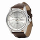 A silver watch with a brown leather strap, featuring a minimalist design and a branded logo.