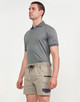 A man wearing a grey polo shirt and beige stretch drill work shorts with a logo. The shorts feature side pockets.