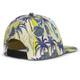 A flat peak cap featuring a patterned design with palm trees and surfboards, primarily in shades of yellow and blue.