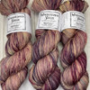 Mad Hatter Hand-Dyed One-of-a-Kind Yarn from Wonderland Yarns. This sport-weight colorway is a variegation featuring a light tan base, with a blending of burgundy, light blue, and brown shades throughout.