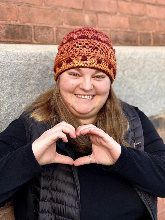 A model shows heart hands while wearing the Tinmel Toque crochet hat pattern shown in a Limited Edition colorway as part of Wonderland Yarns' Blossom Garden Society Yarn Club for 2021.