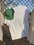 WHITE WHITE SMOKE RESPONSIBLY SOUVENIR TEE ON MESH MERCHANDISE DISPLAY RACK IN URBAN SETTING