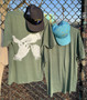 MOSS GREEN WHITE SMOKE RESPONSIBLY SOUVENIR TEE ON MESH MERCHANDISE DISPLAY RACK IN URBAN SETTING