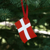 Red and white wooden Denmark flag ornament, red ribbon, hanging on a Christmas tree.