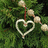 Woven straw heart ornament and star-shaped beads on a garland strung on a green pine tree.