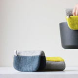 Felt wool potholders in blue-grey, yellow, and grey, one held on a pot handle.