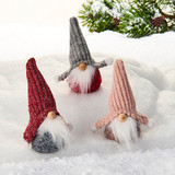 Three fabric gnomes with tall knitted hats in red, grey, and pink on snow.