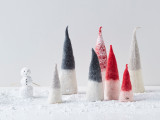 A set of three dark grey felt wool pixies standing on a snow-covered surface.