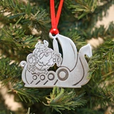 Detailed pewter Viking ship ornament hanging on a Christmas tree by a red ribbon.