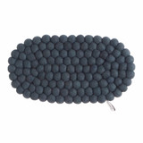 Oval dark grey wool felt ball trivet, viewed from above, with a small brand tag.