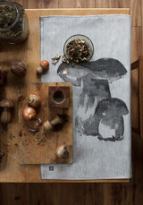 Grey and white organic linen-cotton tea towel with black mushroom illustration on wooden table.