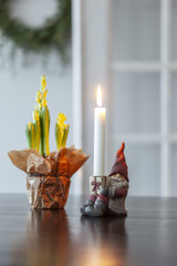 Red-capped tomte figurine holding a lit white candle on a dark tabletop.