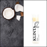 Klinta Coconut Lip Balm stick next to fresh coconut pieces on a dark textured surface.
