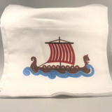 Folded white kitchen towel featuring a brown Viking ship with a red striped sail atop blue waves.