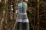 Two colorful, mismatched patterned crew socks worn on legs held up against a blurry forest background.