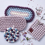 Four handmade felt ball trivets in lavender, blue, and purple, arranged on a light surface with lavender sprigs.