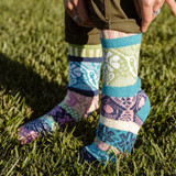 Person standing in green grass wearing mismatched turquoise, pink, green, and blue patterned crew socks.
