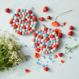 Two round felt wool trivets, red, blue, and white, with strawberries and flowers on a light blue surface.