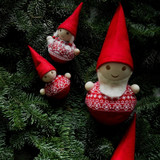 Three wooden Aarikka elf ornaments with red felt hats and knit sweaters on pine branches.