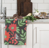 Black organic cotton kitchen towel with red poinsettias, green leaves, and a small bird, hanging on a white cabinet.